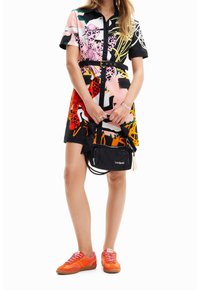 Kortärmad, flerfärgad klänning med blommiga och djurmönster, cinchad midja, tillsammans med en svart axelväska och orangea sneakers.