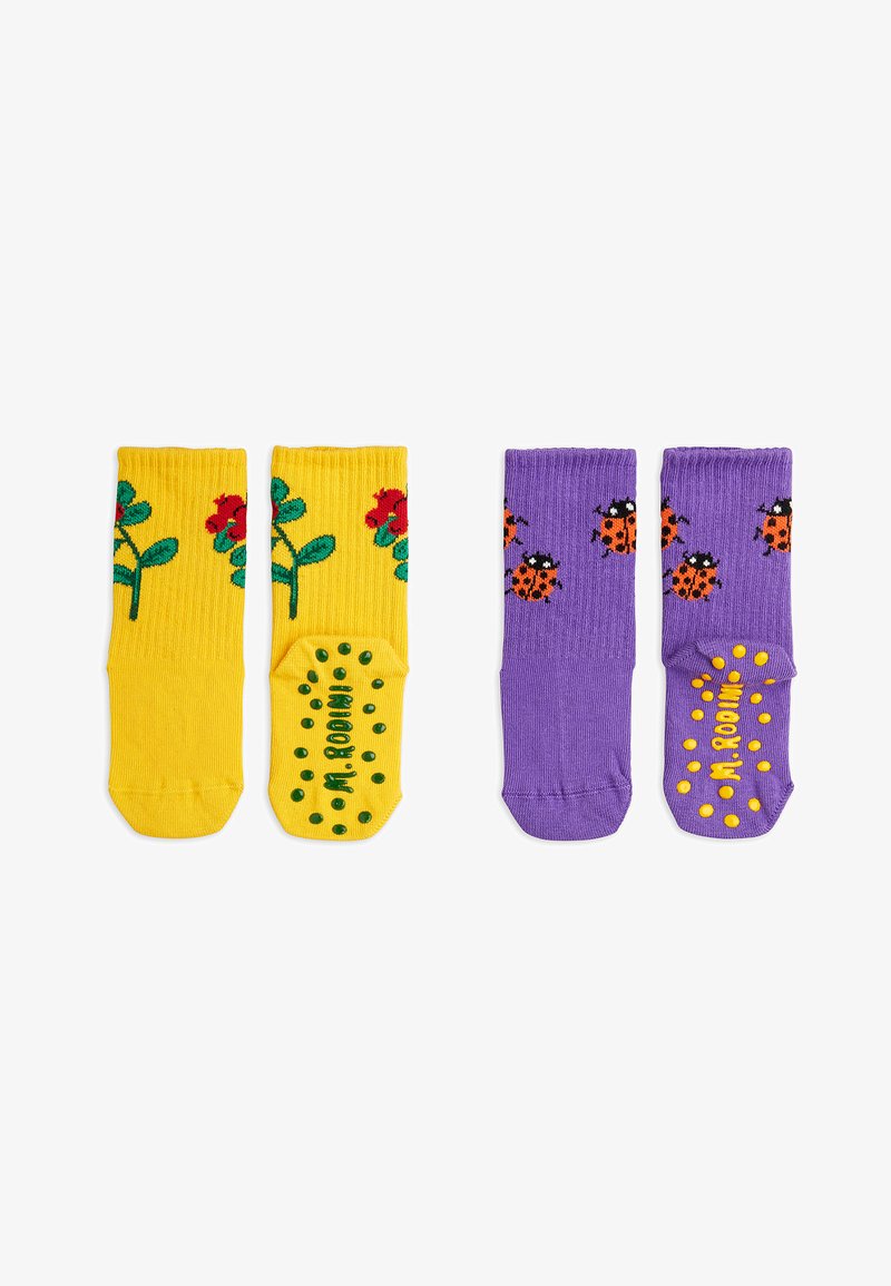 Une paire de chaussettes : l'une est jaune avec des fleurs rouges et des feuilles vertes, l'autre est violette avec des coccinelles noires et orange ; les deux présentent des semelles antidérapantes à pois.