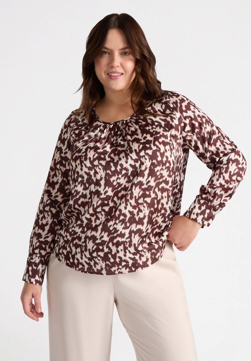 Top a maniche lunghe marrone e crema con un colletto arricciato, abbinato a pantaloni beige chiaro. Tessuto morbido, vestibilità comoda.