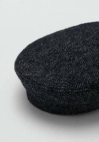Vlnená plochá čiapka s tmavým rybím vzorom, zaobleným tvarom, textúrovanou látkou a mierne zdvihnutým okrajom pre väčší rozmer.