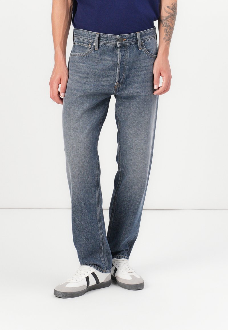 Blauwe denim jeans met een rechte snit, contrasterende stiksels, vijf zakken en een knoopsluiting, gecombineerd met witte sneakers met grijze accenten.