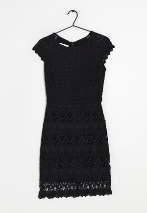 Robe courte en dentelle noire à manches courtes avec motifs floraux, taille ajustée et ourlet festonné, accrochée à un cintre noir sur un fond blanc.