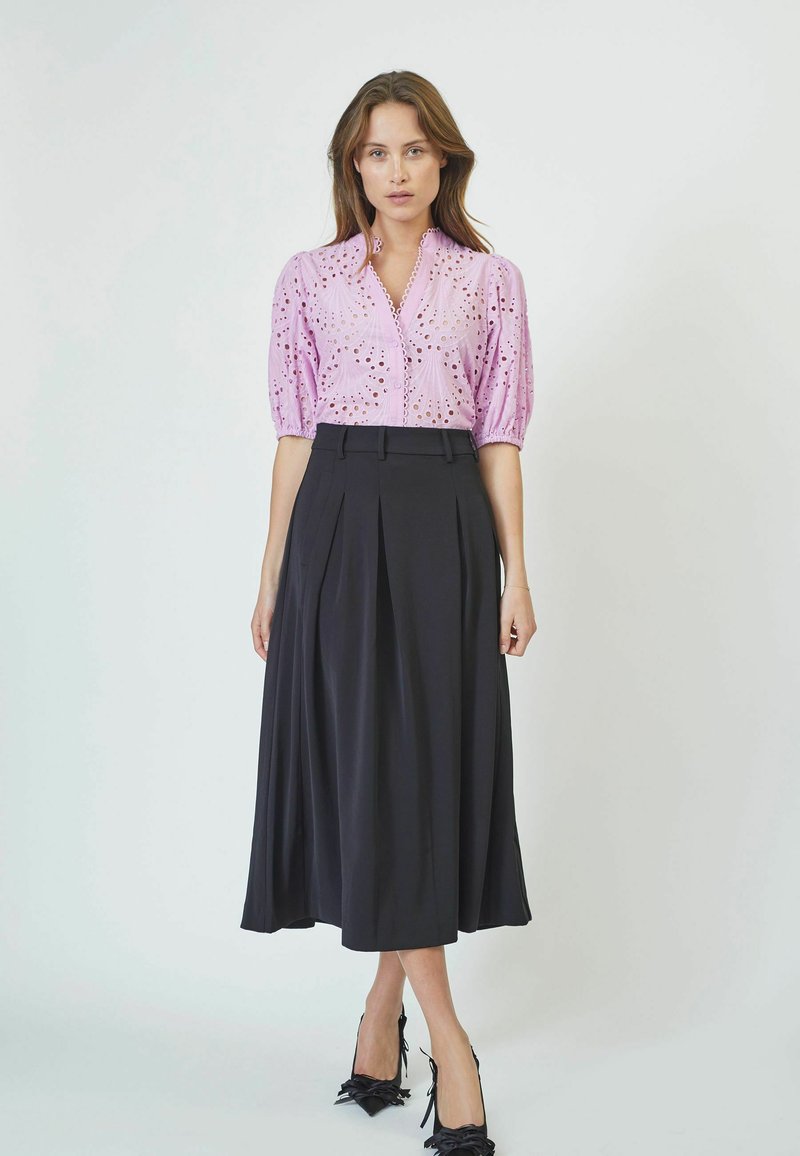Light pink broderie anglaise blouse with puff sleeves paired with a black pleated midi skirt and black pointed-toe heels with bow accents.