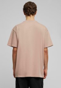 Lyserød t-shirt med kort ærme, afslappet pasform, rund hals og glat bomulds tekstur. Ryggen er ensfarvet uden synlige grafik.