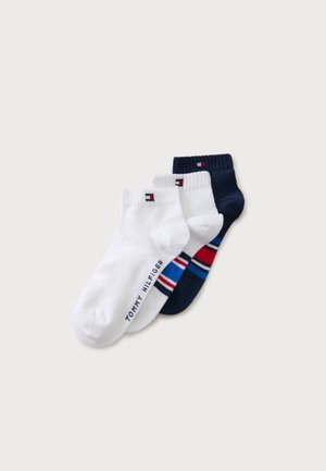Tre par ankelstrømper, to hvide med diskrete flag og branding, et marineblåt med røde, hvide og blå striber, arrangeret overlappende på hvid baggrund.