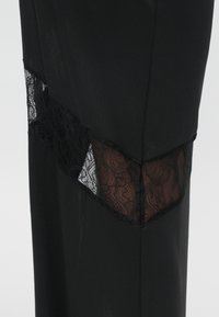 Schwarze Stoffhose mit einem geometrischen Spitzenpaneel an den Seiten, das einen Kontrast von Texturen mit einem transparenten Überzug bietet.