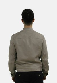 Tan leren jas met een gladde textuur, voorzien van een staande kraag, subtiele perforaties en een getailleerd ontwerp, gezien vanuit de achterkant.