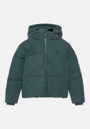 Chaqueta acolchada con capucha en tejido de pana verde oscuro. Cuenta con cremallera frontal, detalle de logo y puños acanalados, con una silueta cuadrada.