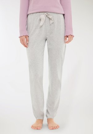 Persona che indossa pantaloni della tuta grigio chiaro con un nastro annodato in vita e piedi nudi, abbinati a una maglietta rosa a maniche lunghe.