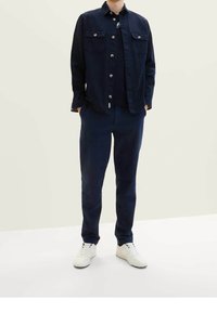 Námořnická modrá košile na knoflíky s dvěma náprsními kapsami, doplněná o námořnické kalhoty a bílé tenisky. Materiál vypadá hladce s volnějším střihem.