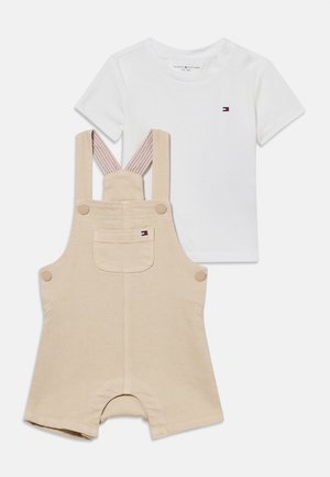 Beežid lühikesed pükspruudid nuppude ja ees taskuga, kombineeritud valge lühikeste varrukatega T-särgiga, millel väike logo rinnal.