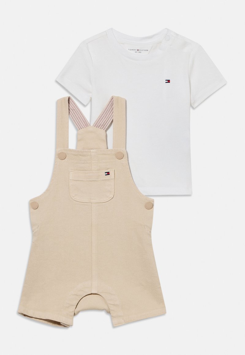 Μπεζ κοντό σαλοπέτα με κουμπιά και μπροστινή τσέπη, συνδυασμένη με λευκό T-shirt κοντό μανίκι με μικρό λογότυπο στο στήθος.