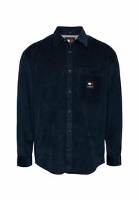 Chemise en velours côtelé bleu marine à manches longues, avec un devant boutonné, une poche poitrine unique et un petit patch logo sur la poche. Tissu texturé.