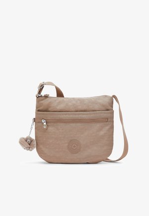 Beige crossbody bag with front zip pocket, adjustable shoulder strap, round logo patch, and attached plush monkey keychain accessory.