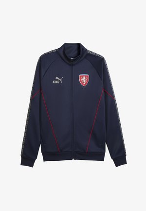 Tumesinine lukuga spordijakk punase äärega, Puma logo, tekst "KING" ning punane kilpembleem kahe lõviga rinnal.