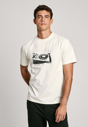 Camiseta de manga corta color crema hecha de algodón, con un estampado gráfico de un tocadiscos en negro. Corte casual con cuello redondo y parte trasera lisa.