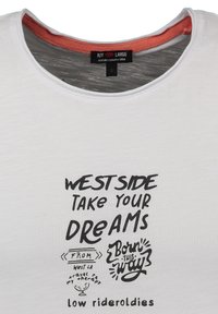 Cuello de camiseta blanca con texto manuscrito en negro: "Lado oeste, lleva tus sueños", "Nacido así" y "oldies de low rider" en diferentes tipografías.