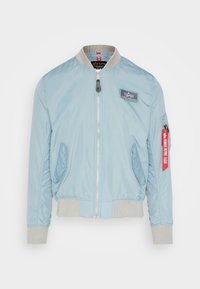 Light blue bomber jacket made of smooth nylon. Features a zip front, ribbed cuffs and hem, and a patch on the chest with a red accent tag.