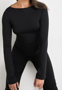 Schwarzes, eng anliegendes Langarmoberteil mit einem Bootsausschnitt, kombiniert mit hochgeschnittenen schwarzen Hosen. Glattes, dehnbares Material, minimalistisches Design.