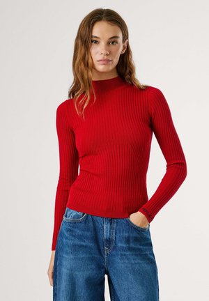 Punane ribadega pikkade varrukatega särk, millel on kõrge kaelus, figuuri rõhutav disain ja diskreetne logo detail varrukal. Kombineeritud lõtvade denimitega.