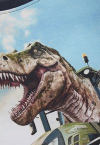 Grafische T-shirt met een gedetailleerde, kleurrijke afdruk van een brullende dinosaurussen tegen een blauwe lucht met een voertuig op de voorgrond.