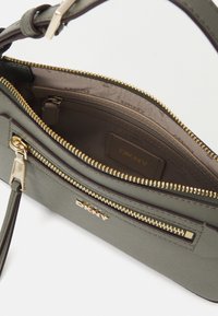 Borsa a mano verde oliva realizzata in tessuto testurizzato con dettagli in metallo dorato, caratterizzata da una chiusura con zip, diversi scomparti e una placca con logo all'interno.