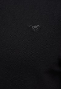 Tissu noir texturé avec un petit logo de cheval gris foncé brodé au centre.
