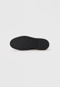 Black shoe sole with textured surface and smooth toe; contoured design with slight arch. Minimal details and no visible branding.