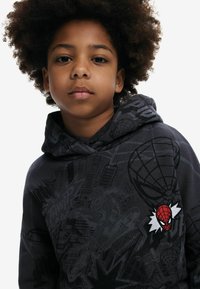 Zwarte hoodie met een Spider-Man patch en grafisch ontwerp in stripstijl. Gemaakt van zachte stof met een ontspannen pasvorm en een gestructureerd oppervlak.