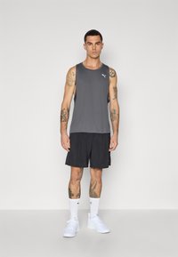 Grå atletisk tanktop med rund halsudskæring, parret med sorte shorts. Hvidt logo på brystet, båret med hvide sneakers og sokker.