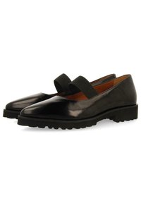 Scarpe in pelle nera con finitura lucida, dotate di punta affilata e due fasce elastiche nere sulla parte superiore. Suola in gomma testurizzata.
