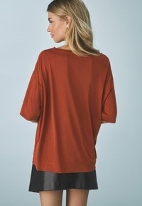 Roodbruine oversized t-shirt met korte mouwen, een soepele textuur, afgewerkte zomen en een relaxed fit, gecombineerd met een zwarte leren minirok.