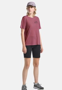 Chemise courte à manches maroon avec un graphique sur la poitrine, associée à un short noir et des chaussures de randonnée grises. Une casquette gris clair complète la tenue.