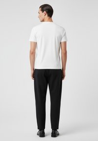 Camiseta blanca de manga corta combinada con pantalones negros de corte ajustado. El conjunto tiene una textura suave y un diseño simple y minimalista.