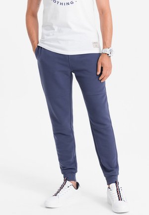 Marineblauwe joggingsbroek van gestructureerde stof, met een aansluitend ontwerp en elastische boorden, gecombineerd met witte sneakers en een wit T-shirt.