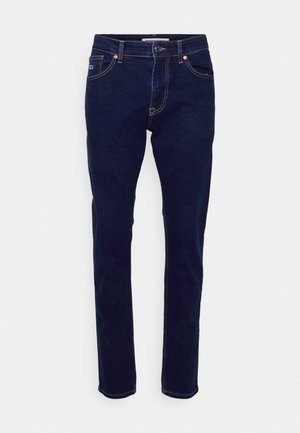 Tamno plavi traperice s uskim krojem, dizajnom s pet džepova, bakrenim zakovicama i pojasom. Tkanina ima gladak tekstur.