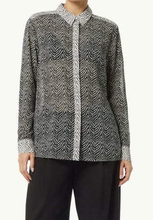 Langærmet bluse med zebra print, skjulte knapper, krave og hvide manchetter, båret med sorte bukser med vide ben.