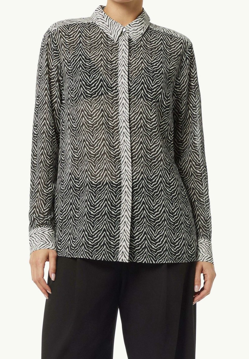Blouse manches longues imprimé zèbre avec patte de boutons dissimulée, col et poignets blancs, portée avec un pantalon noir à jambes larges.