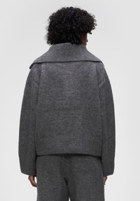 Szary sweter dziany z wysokim kołnierzem, luźnym krojem, ściągaczem u dołu i opadającymi ramionami, charakteryzujący się miękką teksturą.