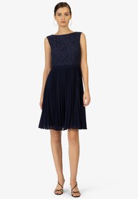 Robe bleu marine avec un corps en dentelle, sans manches, et une jupe plissée. Accentuée d'une taille cintrée et d'un détail d'ourlet transparent.