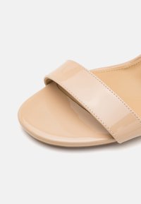 Sandal in vernice nuda con fascia ampia e lucida e punta aperta arrotondata. La soletta beige morbida completa il design. Texture liscia.