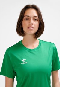 Zielona sportowa koszulka wykonana z gładkiej tkaniny. Posiada prążkowany, okrągły dekolt oraz białe logo Hummel na lewej stronie klatki piersiowej.