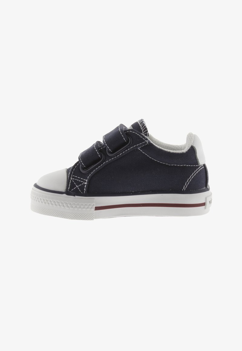 Marineblauwe canvas sneaker met witte rubberen neuskap en zool, twee klittenbandsluitingen en contrasterende witte stiksels.