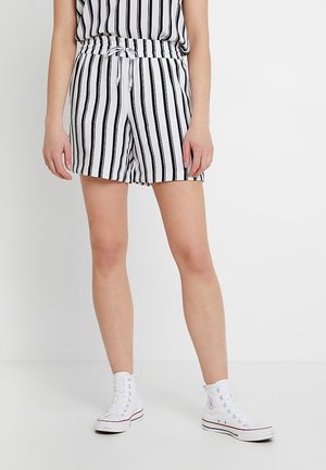 Shorts à rayures noires et blanches avec une taille élastique et un cordon de serrage. Portés avec des baskets montantes blanches. Tissu texturé.