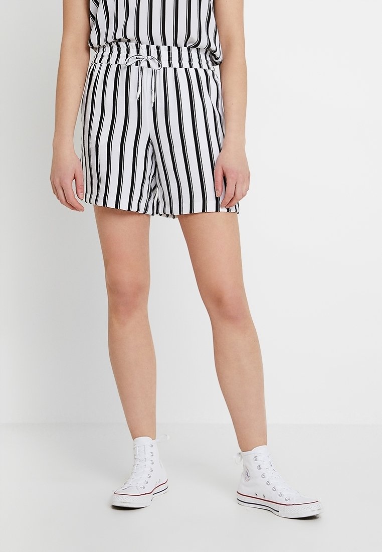 Shorts à rayures noires et blanches avec une taille élastique et un cordon de serrage. Portés avec des baskets montantes blanches. Tissu texturé.