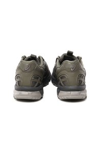 Olijfgroene sportschoenen met een gestructureerd oppervlak, grijze accenten, een ondersteunende hak en een uniek tussenzoolontwerp voor demping en stabiliteit.