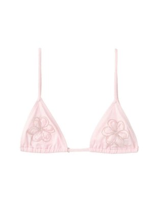 Femeie în bikini alb și acoperire croșetată stând la marginea unei piscine, cu vegetație tropicală luxuriantă în fundal.