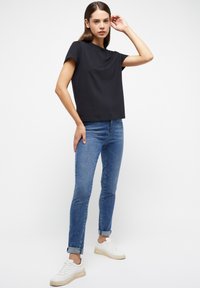 T-shirt nera a maniche corte con scollo rotondo abbinata a jeans skinny blu e sneakers bianche. Design semplice con vestibilità comoda.