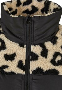 Zwarte ritsjack met een hoge kraag, afgewerkt met een beige en zwart dierenprint fleece stof aan de bovenkant en een gladde zwarte stof aan de onderkant.