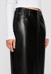 Zwarte leren rok met een rechte snit, een gladde textuur, een voorzak met een gegraveerd logo en subtiele stiksels.